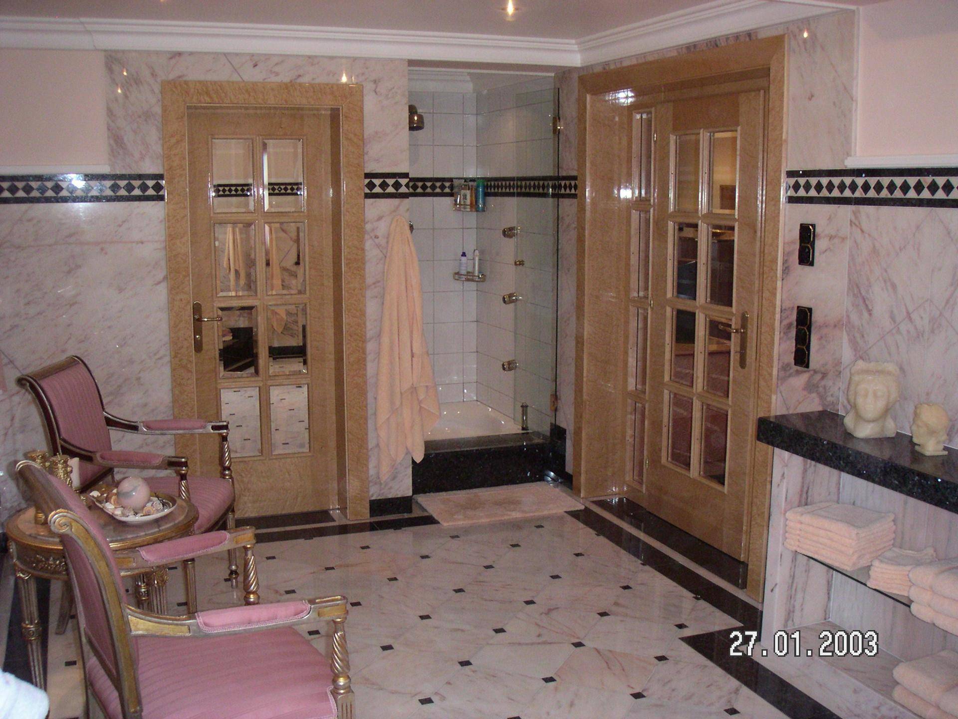 Geräumiges Badezimmer mit Sitzgelegenheiten, Marmorwänden und einer begehbaren Dusche.