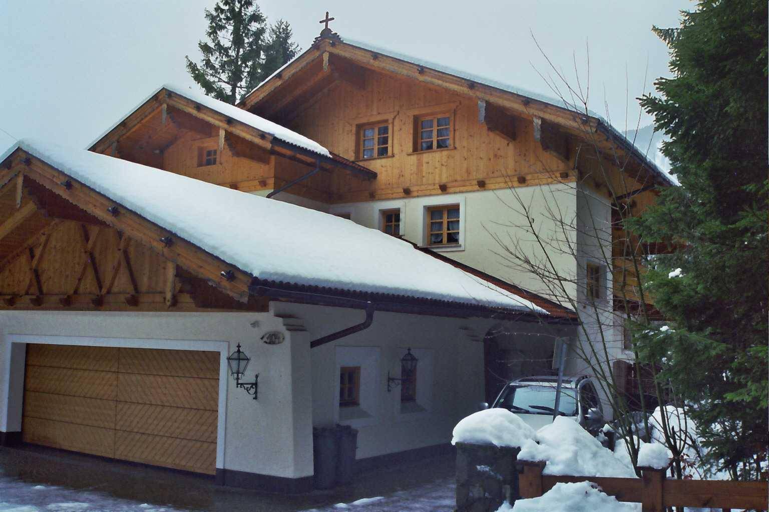 Traditionelles Haus mit Holzfassade, schneebedecktem Dach und integrierter Garage.