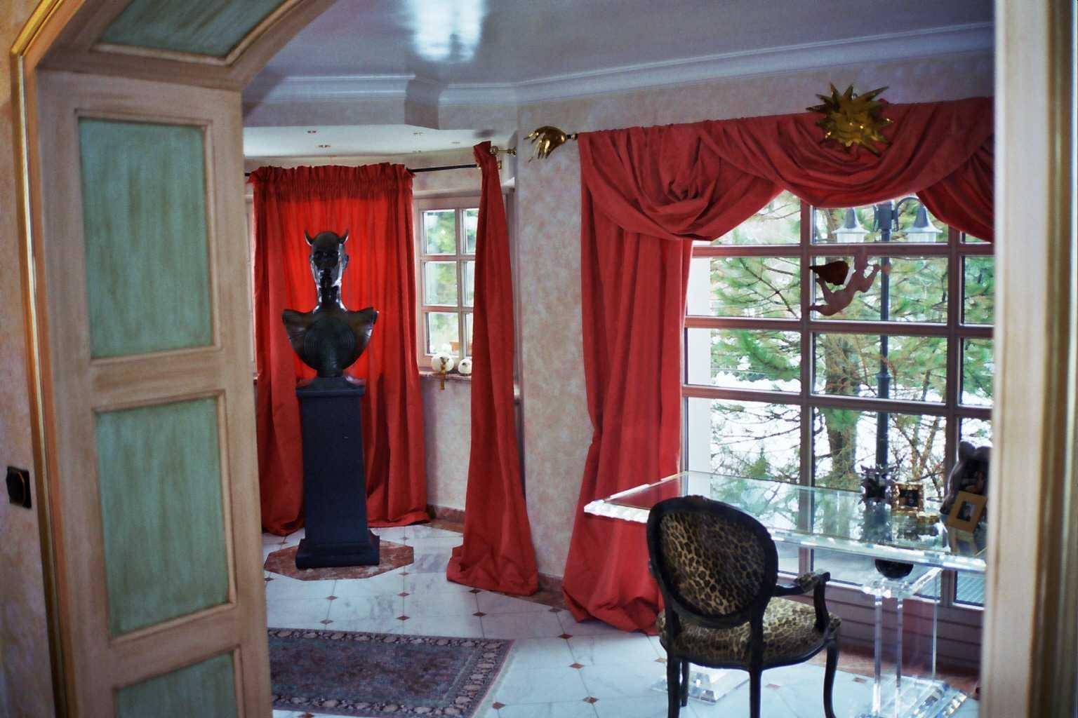 Heller Raum mit Glastisch, auffälligem Stuhl und roten Vorhängen, mit Blick nach draußen.