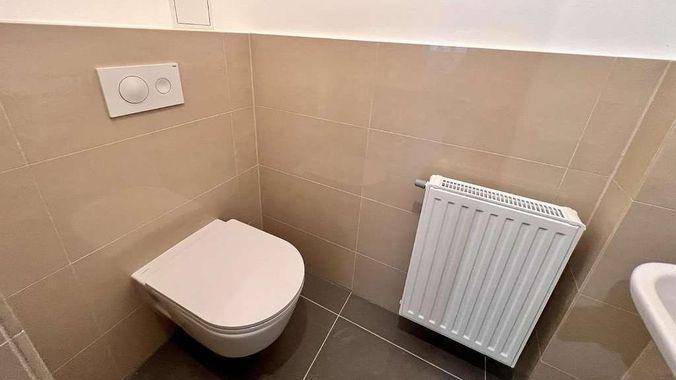 Kompakte Gästetoilette mit wandhängendem WC, Heizkörper und beigefarbenen Wandfliesen.