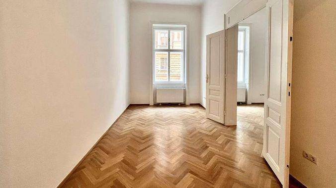 Geräumiger Raum mit elegantem Fischgrätparkett und einem großen Fenster, das den Raum erhellt.