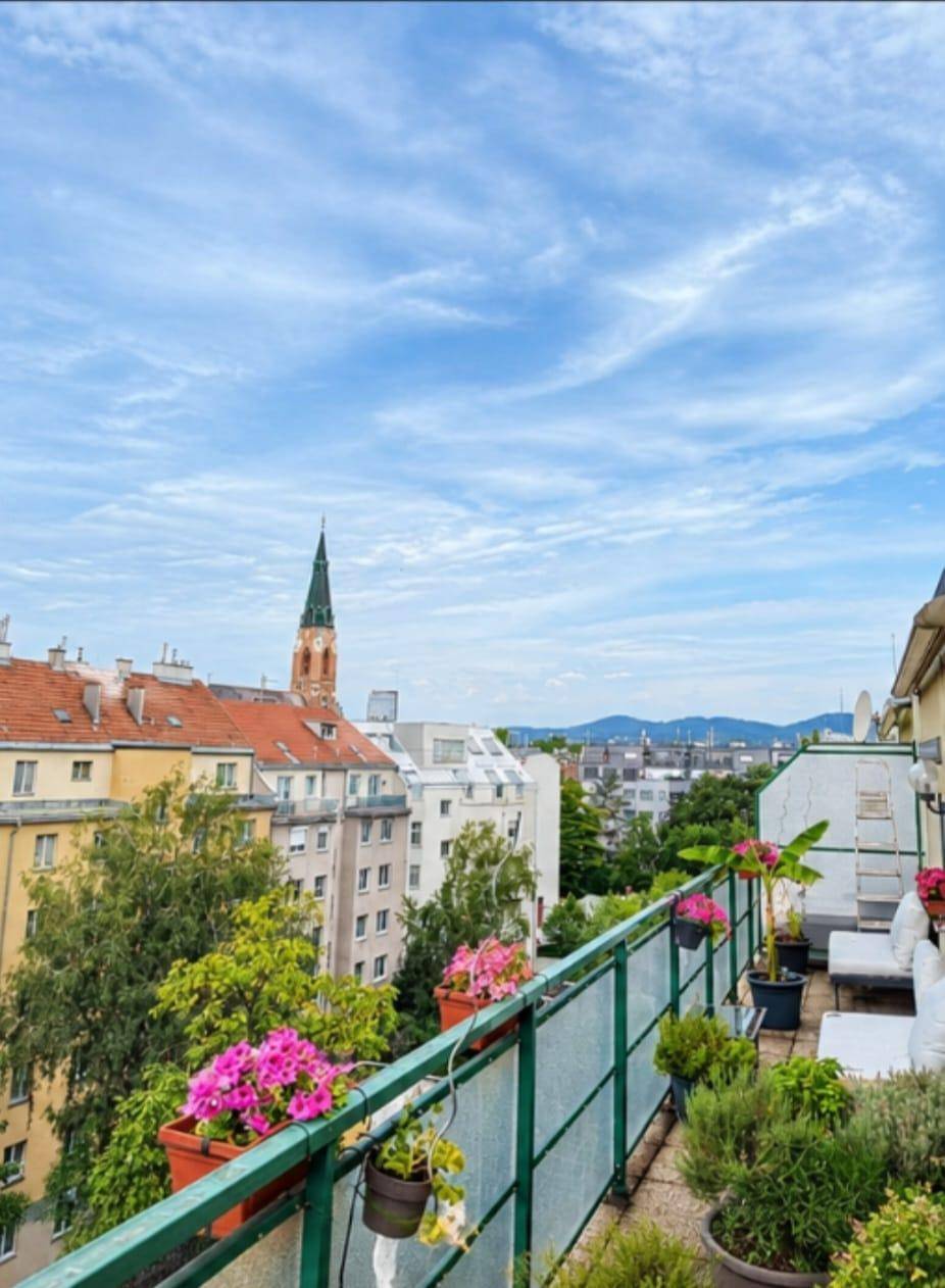 Balkon mit weitem Blick über die Stadt, Kirchturm und entfernte Berge unter blauem Himmel.