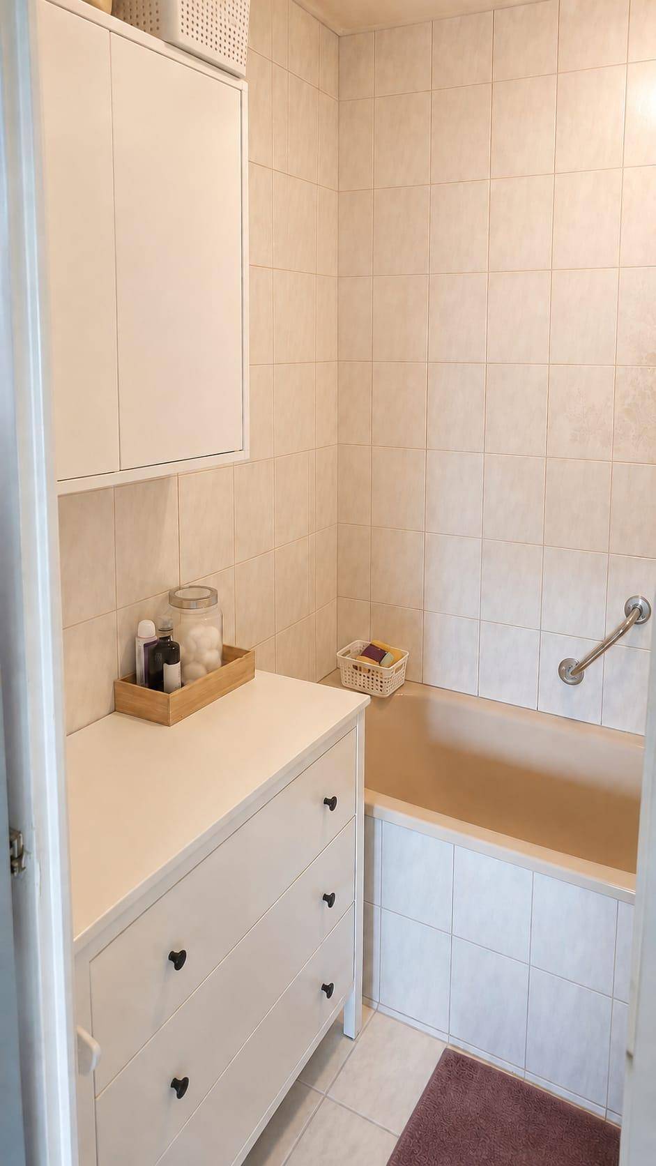 Badezimmer mit Badewanne, hellen Fliesen und einem Schrank für persönliche Gegenstände.