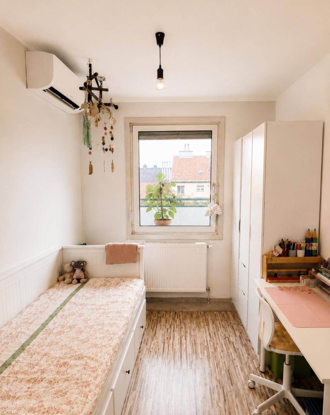 Helles Kinderzimmer mit Einzelbett, Schreibtisch, Schrank und Klimaanlage unter dem Fenster.