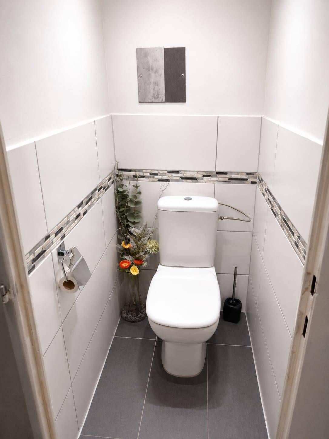 Separates WC mit modernen Fliesen, Toilette und dezenter Dekoration an der Wand.