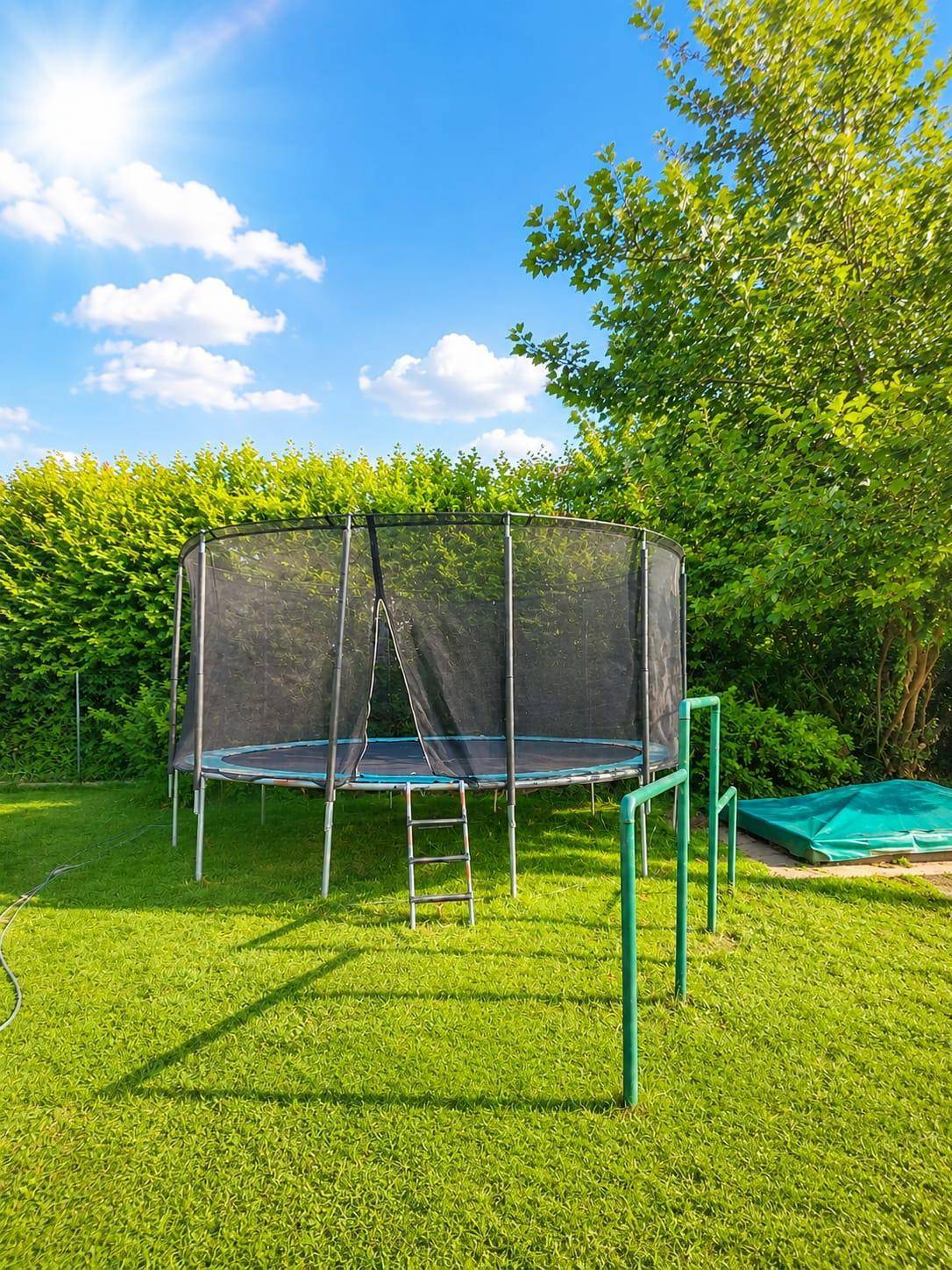 Sonniger Gartenbereich mit großem Trampolin auf einer gepflegten Rasenfläche und Hecke.