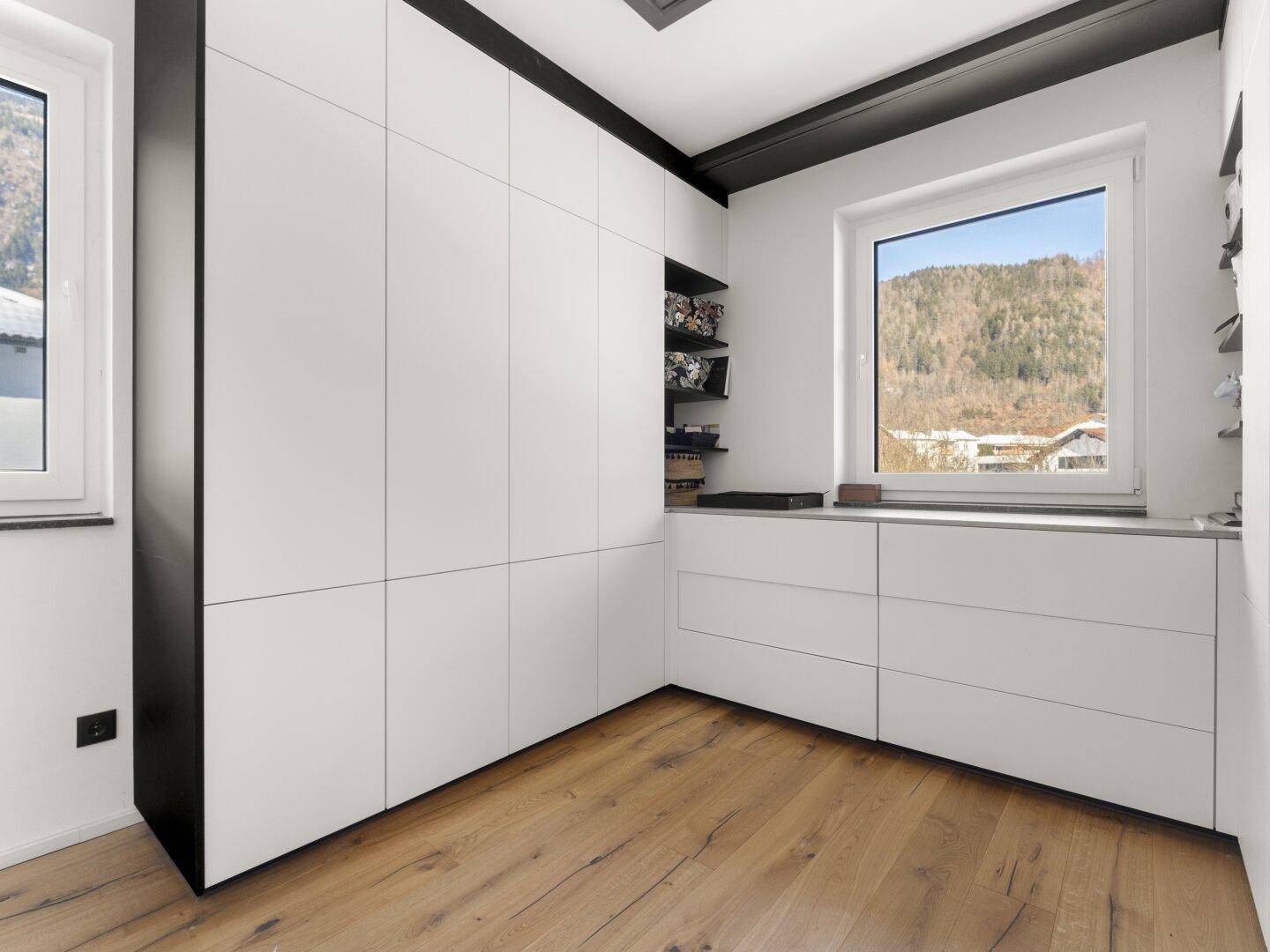 Schlafzimmer mit Einbauschränken, Holzboden und Bergblick durch das Fenster.