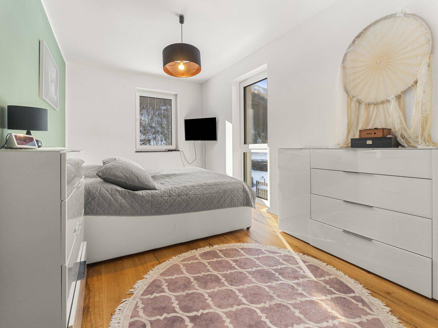 Helles Schlafzimmer mit Holzboden, modernen Möbeln und Blick ins Grüne.