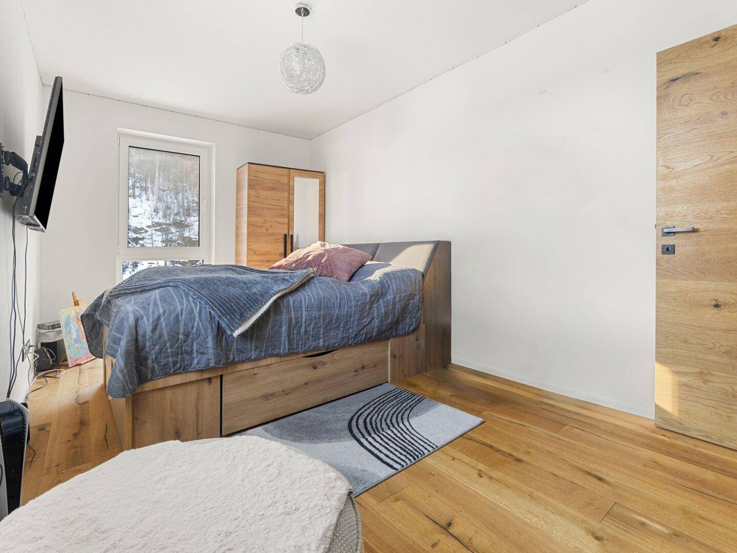 Schlafzimmer mit Holzboden, Holzbett und Blick auf die verschneite Landschaft.