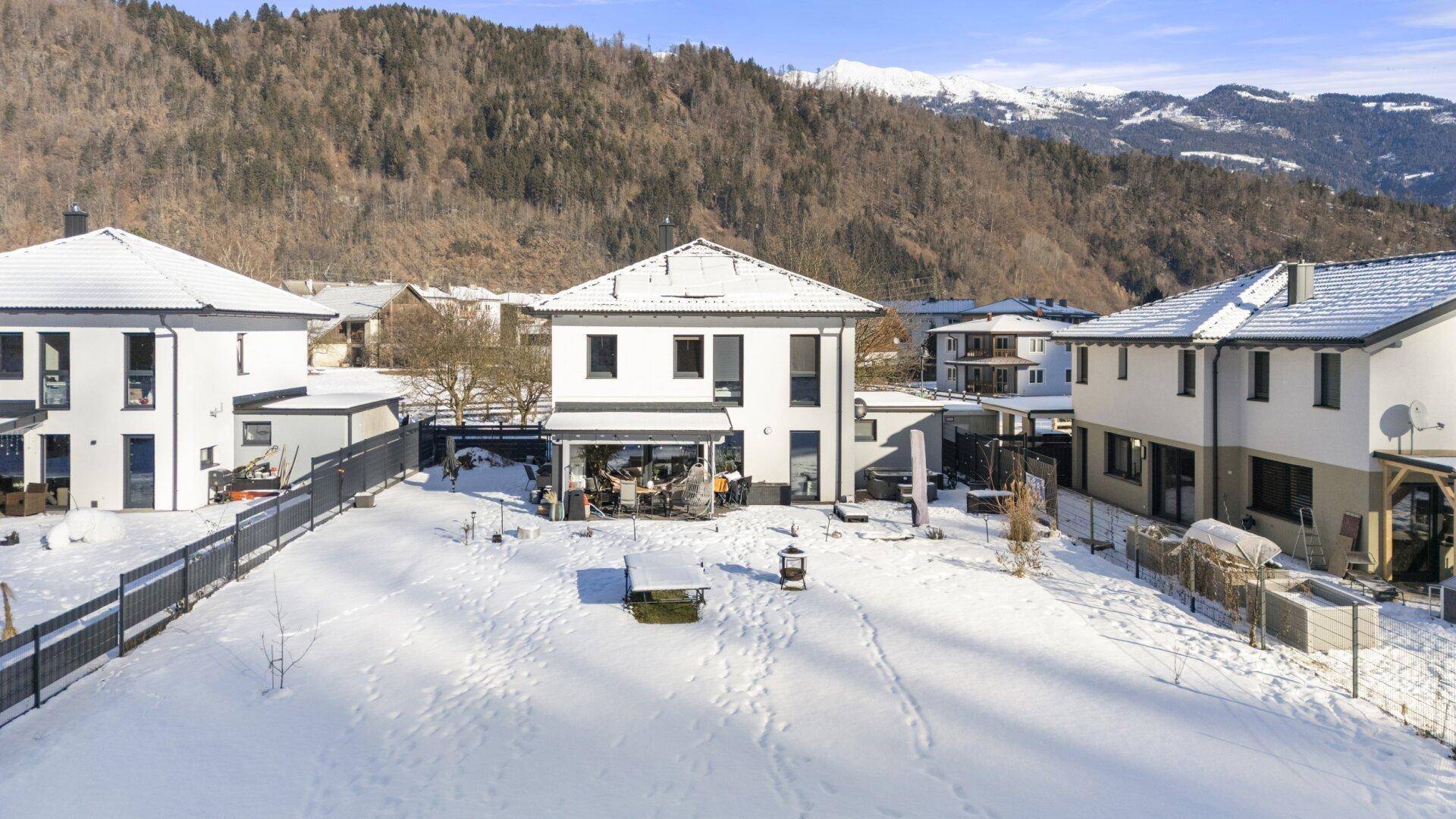 Großzügiger Gartenbereich mit Terrasse und Einfamilienhaus in winterlicher Berglandschaft.