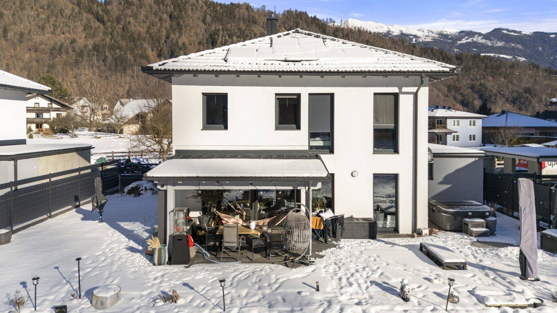Überdachte Terrasse mit Sitzgelegenheiten und Blick auf den verschneiten Garten.
