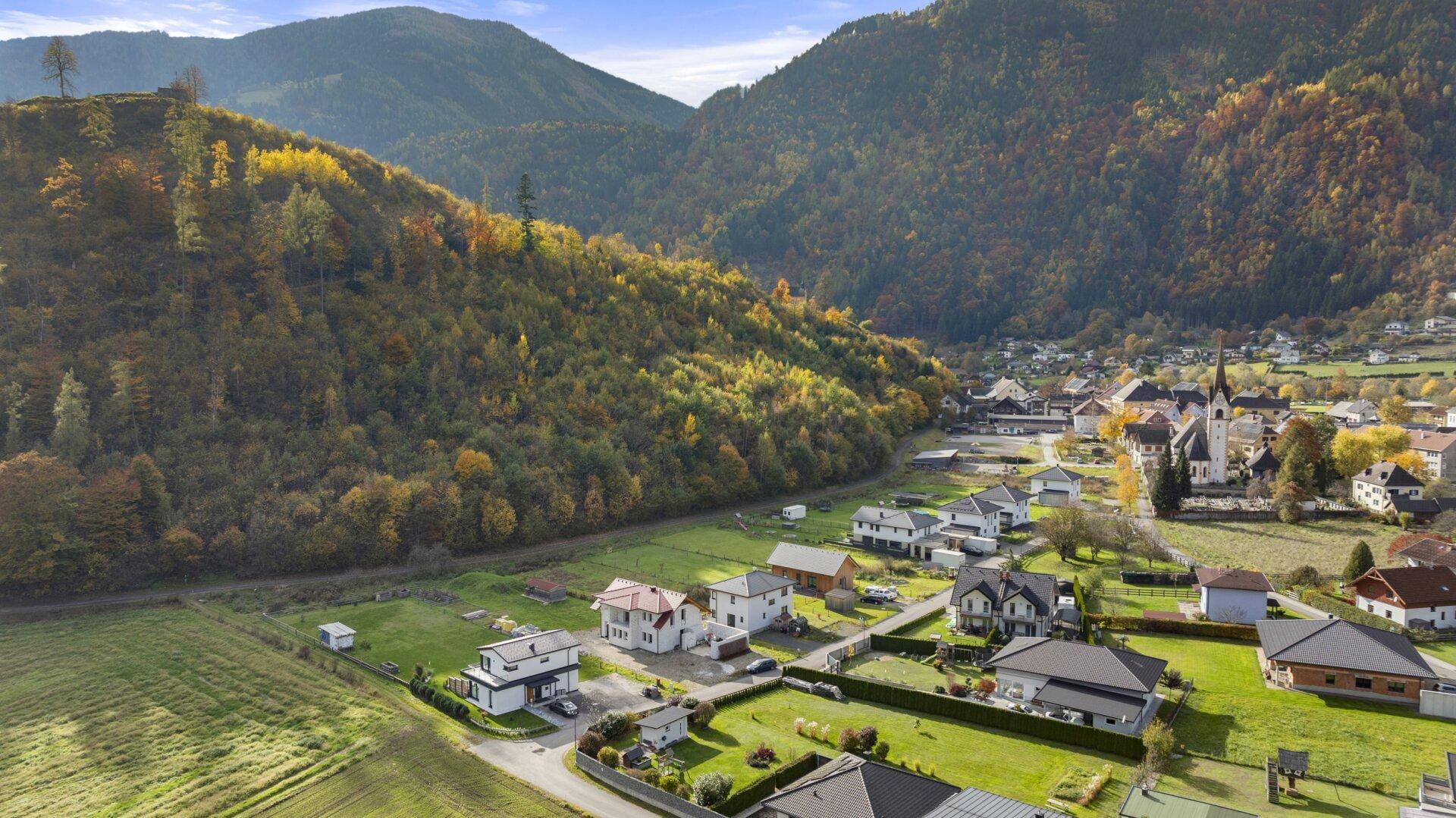 Panoramablick auf ein Dorf in einem Tal, umgeben von herbstlichen Bergen.
