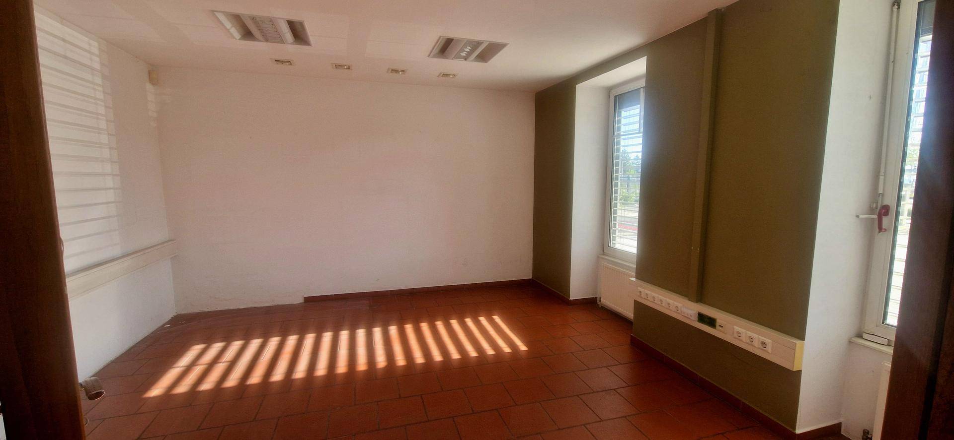 Heller Büroraum mit Fliesenboden und einem Fenster mit Jalousien.