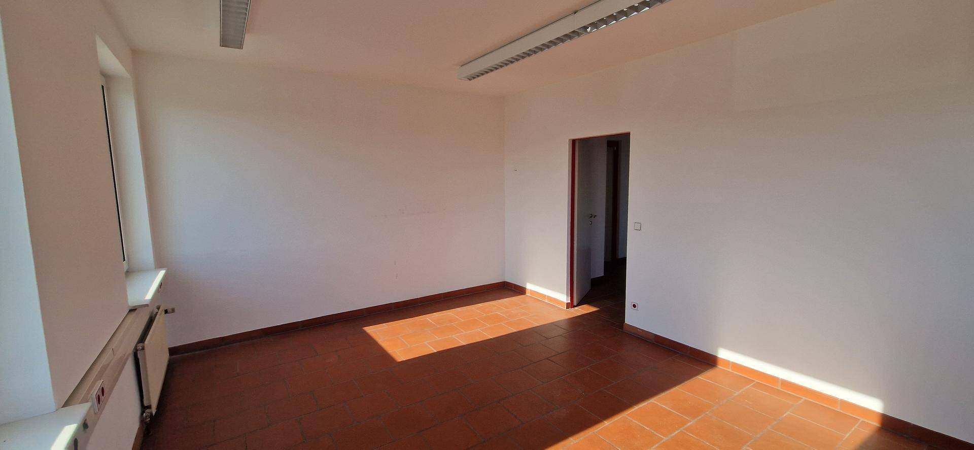 Leerer Büroraum mit Terrakotta-Fliesenboden und weißen Wänden, der von der Sonne durchflutet wird.