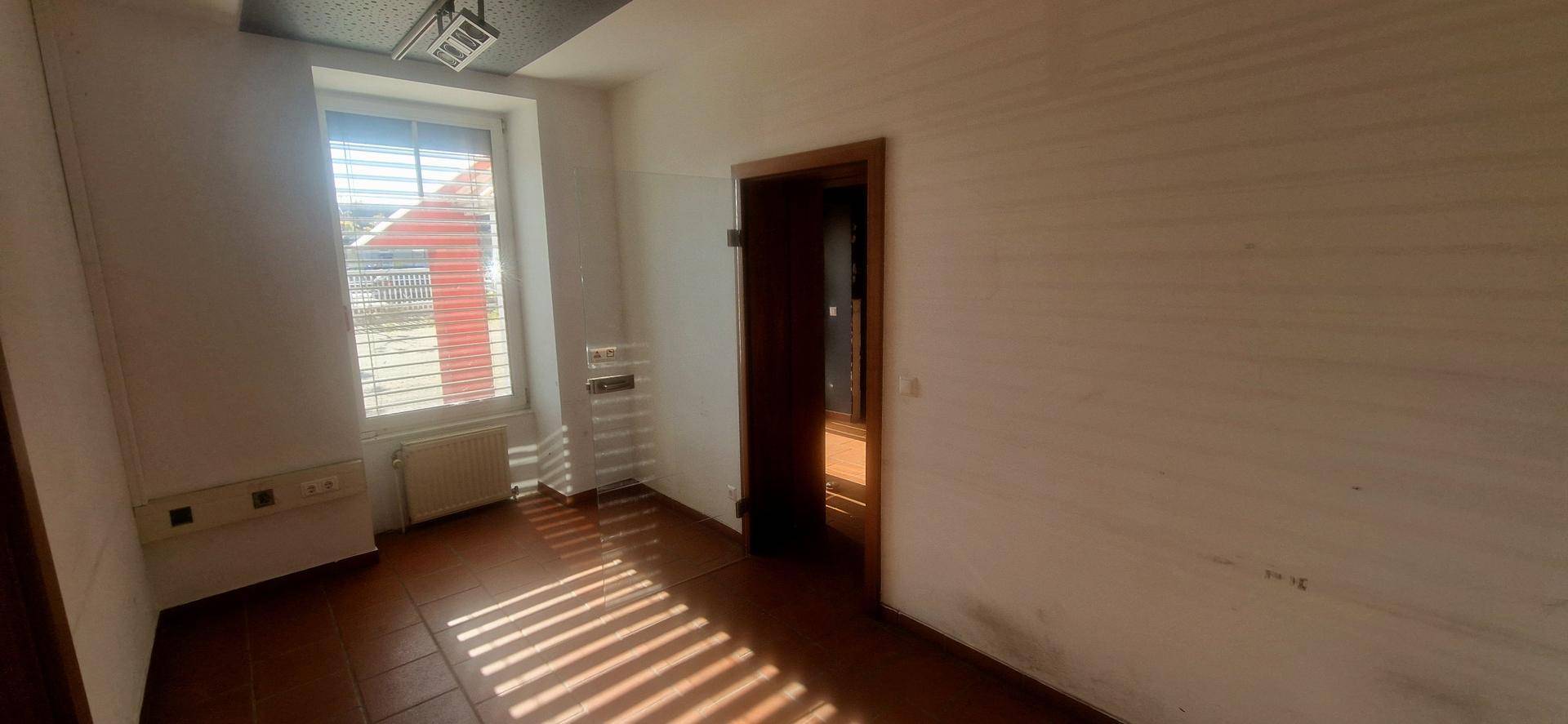 Kleiner Büroraum mit Fenster, Heizkörper und dunklem Fliesenboden.