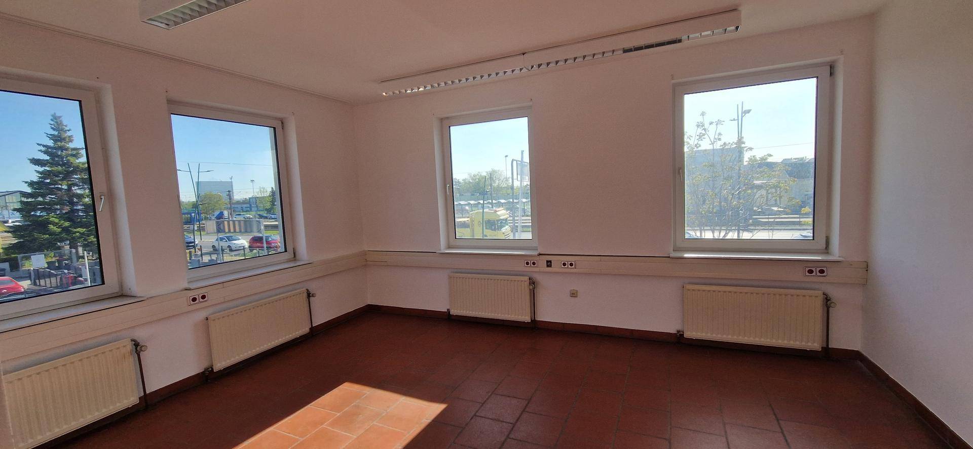 Helles Büro mit Terrakotta-Fliesenboden und mehreren Fenstern, die einen Blick auf die städtische Umgebung bieten.