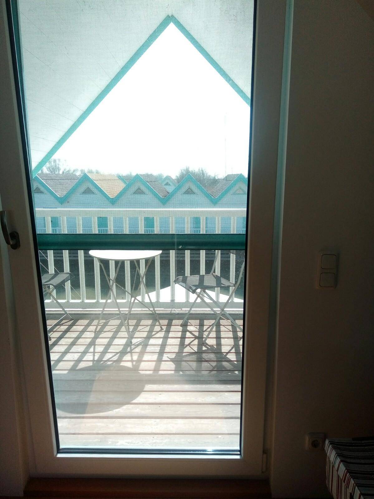 Blick durch die Balkontür auf eine kleine Terrasse mit Sitzgelegenheiten und die charakteristischen Häuser am Wasser.