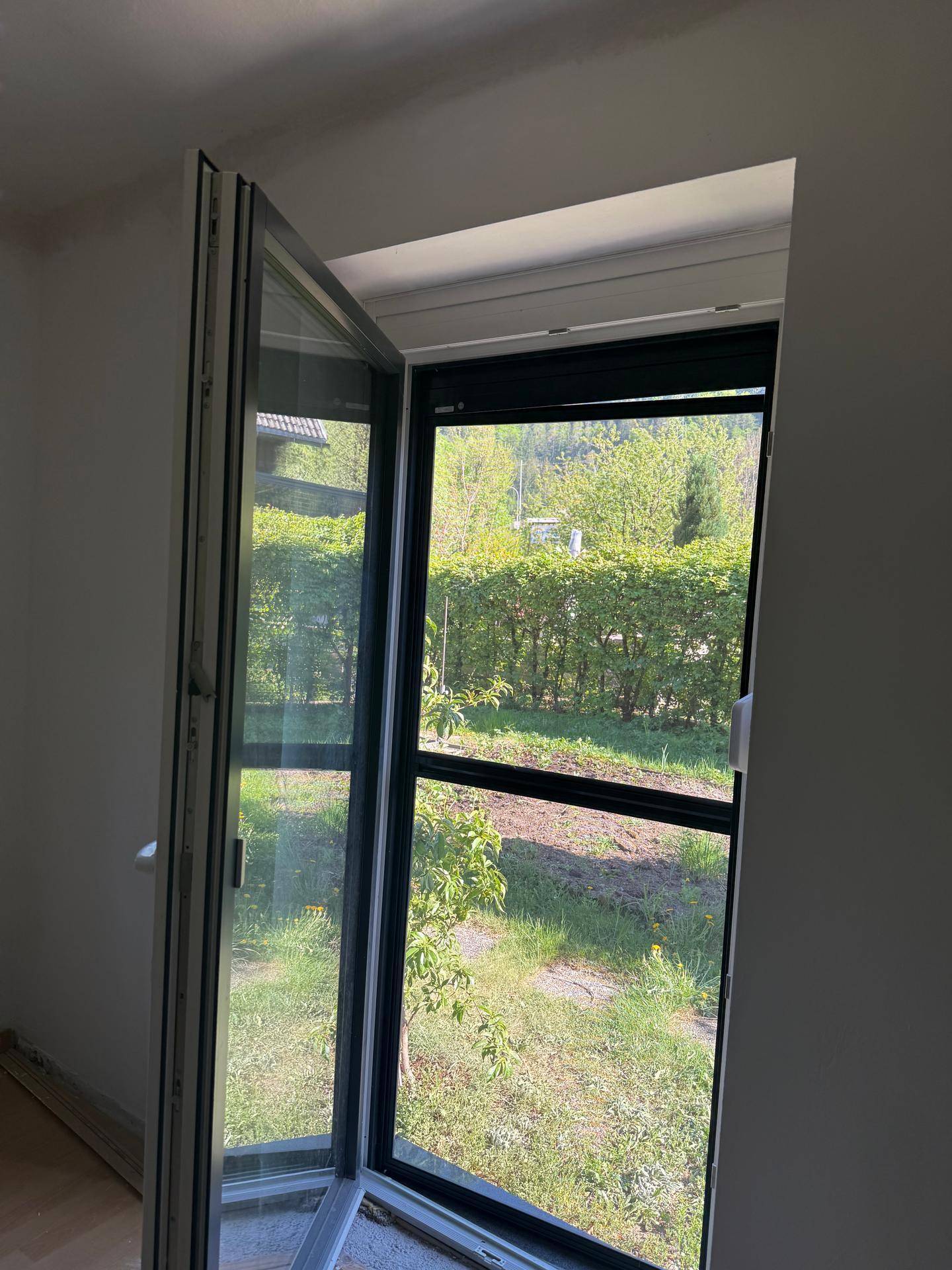 Geöffnetes Fenster mit Blick auf eine grüne Hecke und den Gartenbereich.