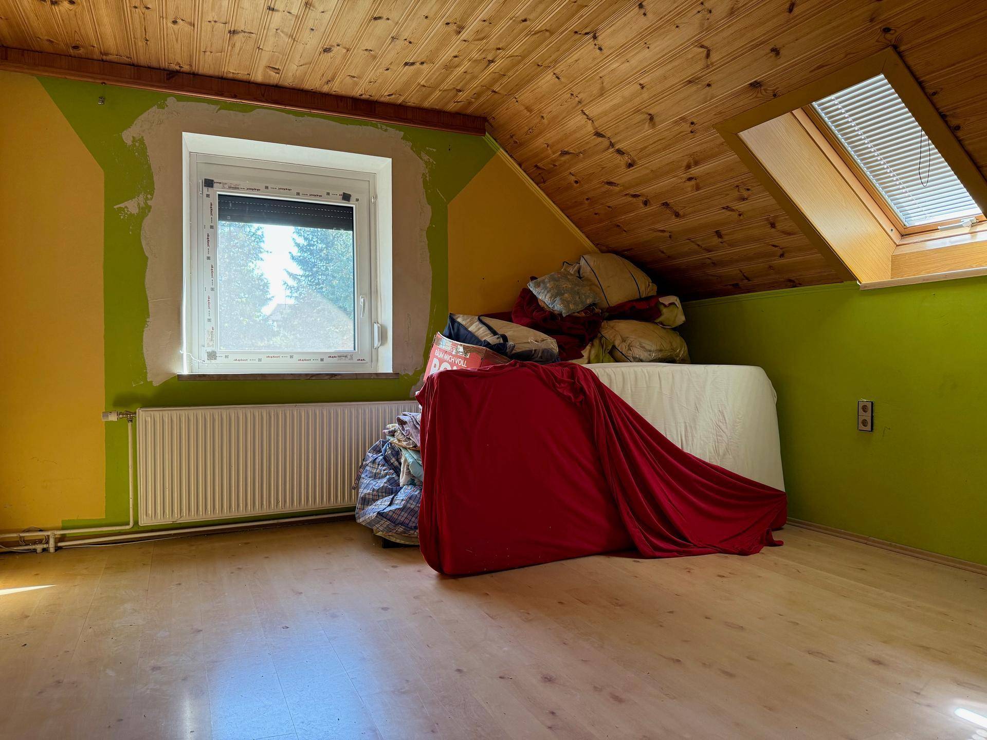 Dachzimmer mit schrägen Holzdecken, grün gestrichenen Wänden und einem Dachfenster.