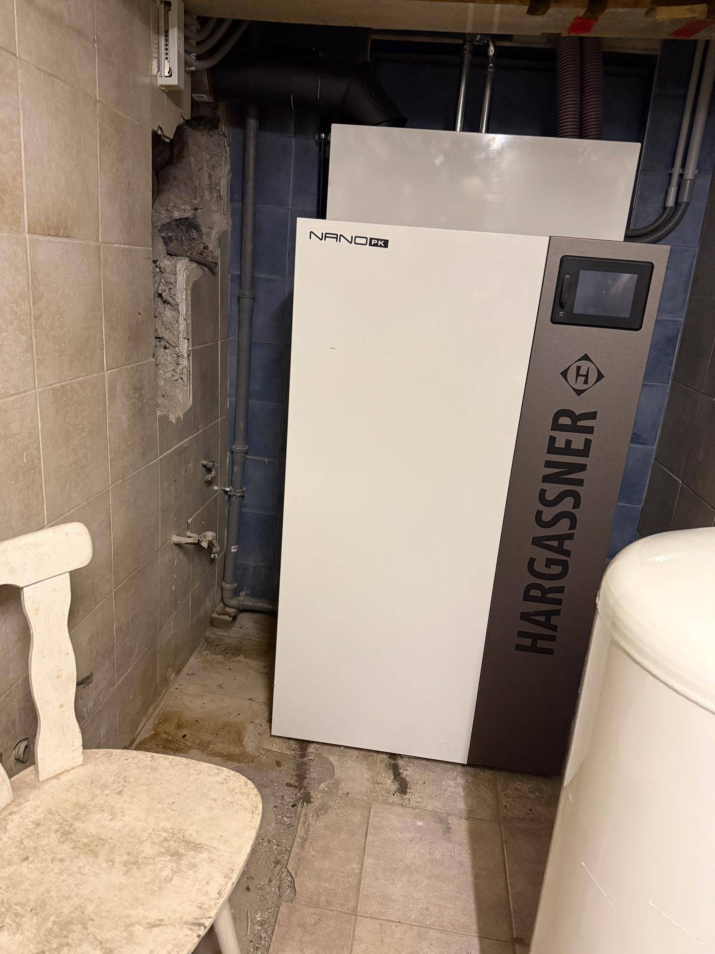 Heizungsraum im Keller mit einem modernen Hargassner Heizsystem und gefliesten Wänden.