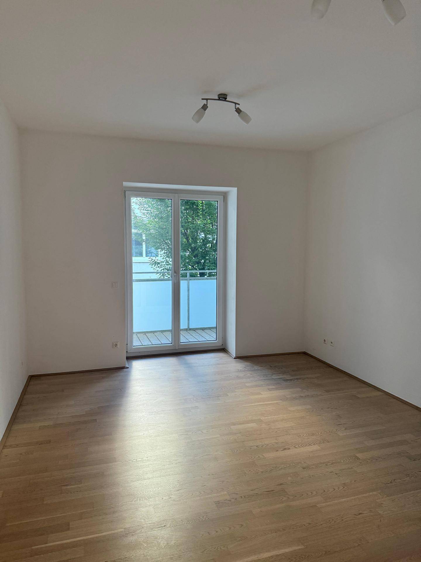 Lichtdurchflutetes Wohnzimmer mit Balkontür und Blick ins Grüne.