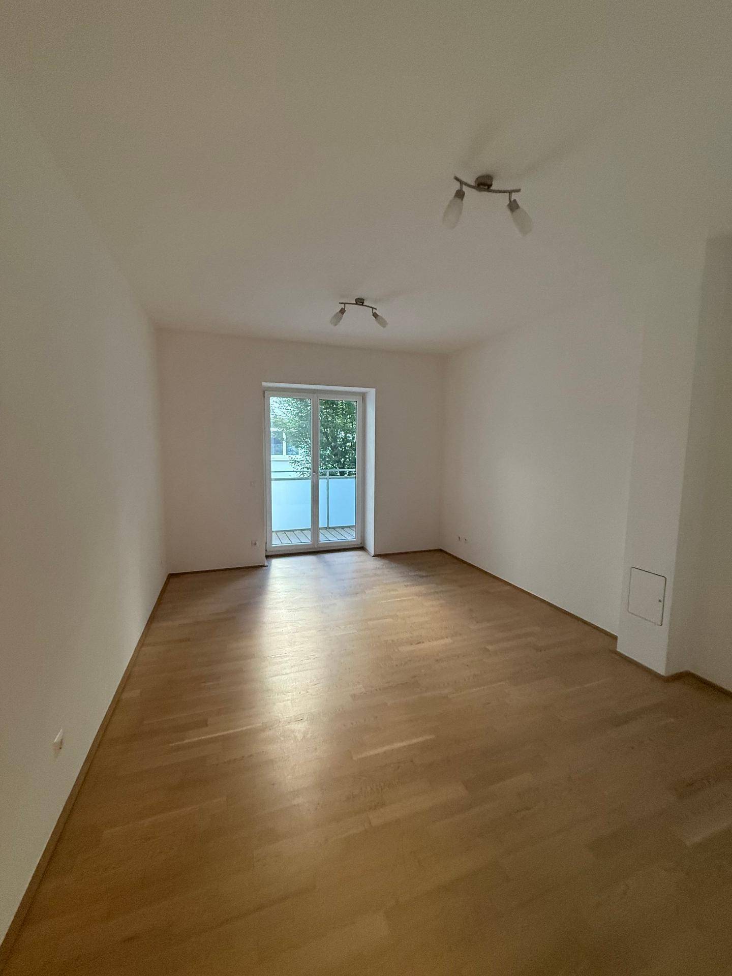 Helles Wohnzimmer mit Holzfußboden und direktem Zugang zu einem Balkon.