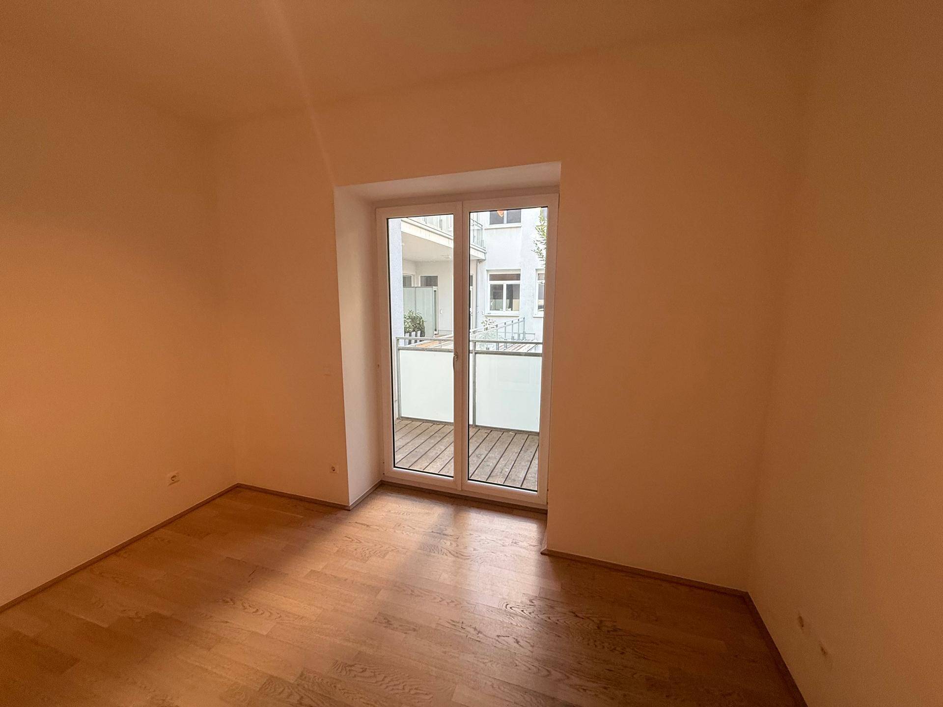 Helles Zimmer mit Holzfußboden und Balkonzugang mit Blick auf den Innenhof.
