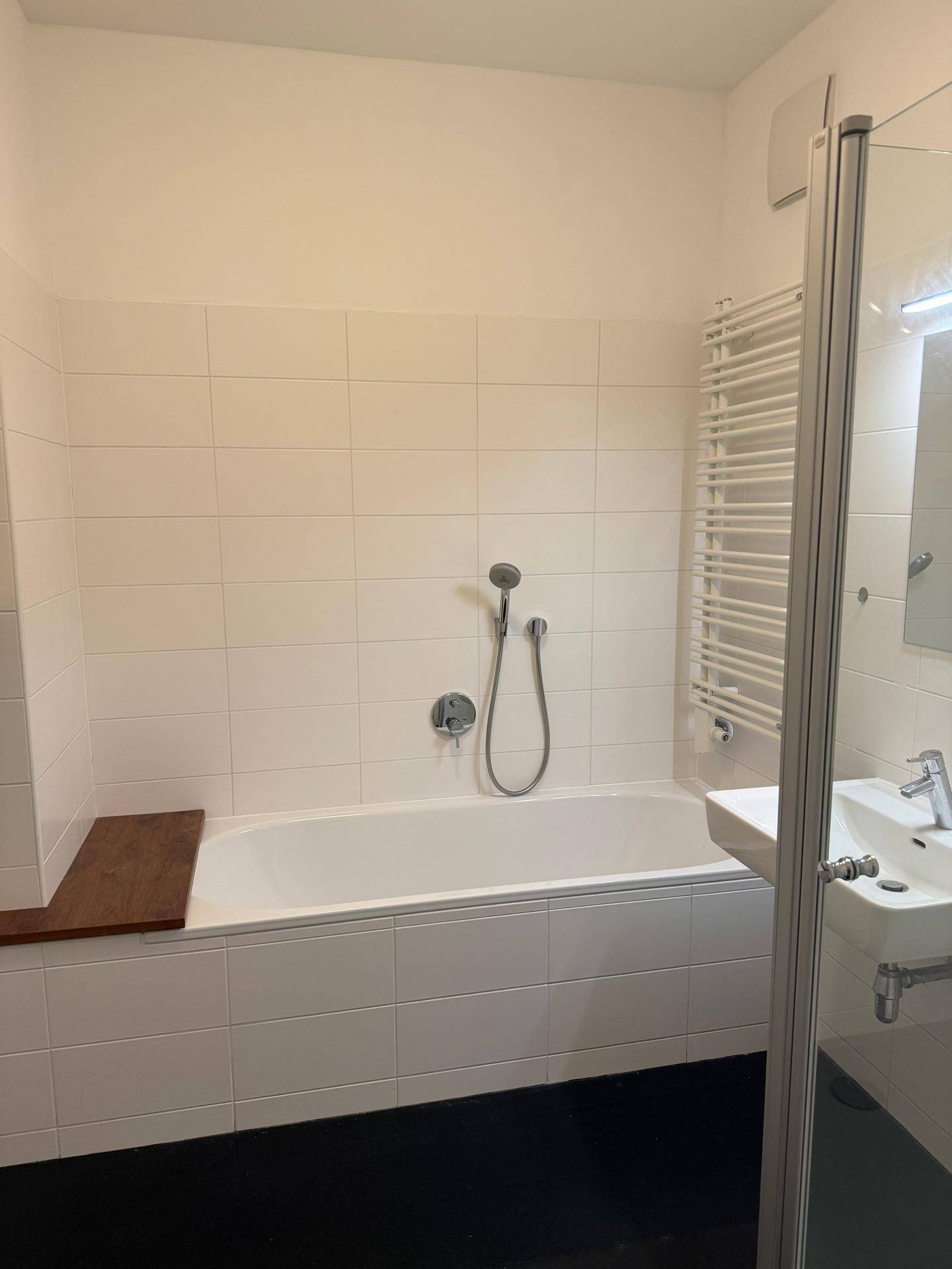 Modernes Badezimmer mit Badewanne, Duschbereich, Einzelwaschbecken und beheiztem Handtuchhalter.