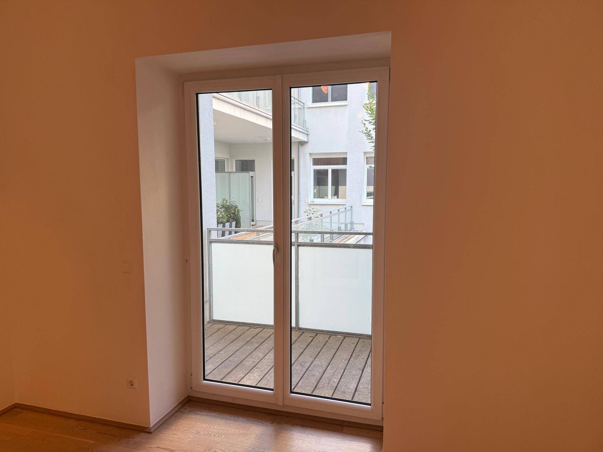 Balkon mit Holzboden und Blick auf den ruhigen Innenhof des Gebäudes.