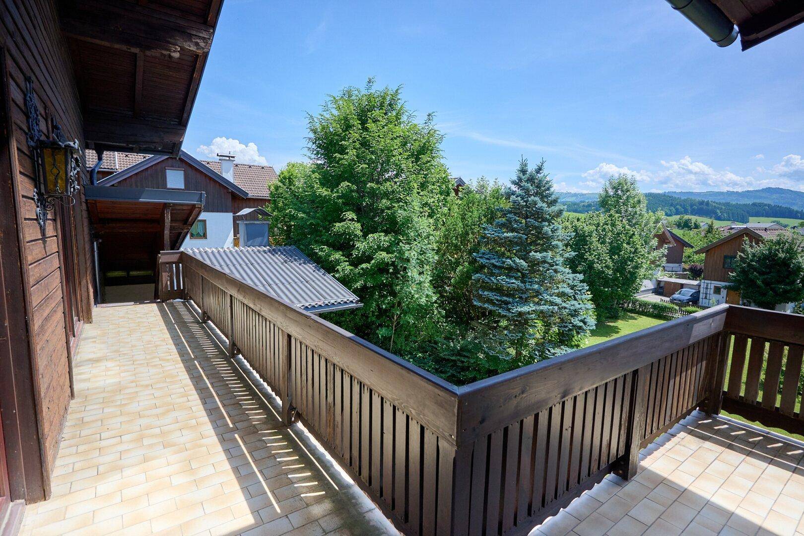 Geräumiger Balkon mit Holzgeländer und Fliesenboden, umgeben von Bäumen mit weitem Blick.