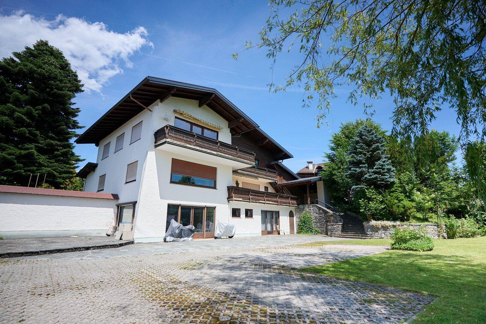 Ansicht des Hauses mit großer gepflasterter Auffahrt und angrenzendem Rasenbereich unter blauem Himmel.