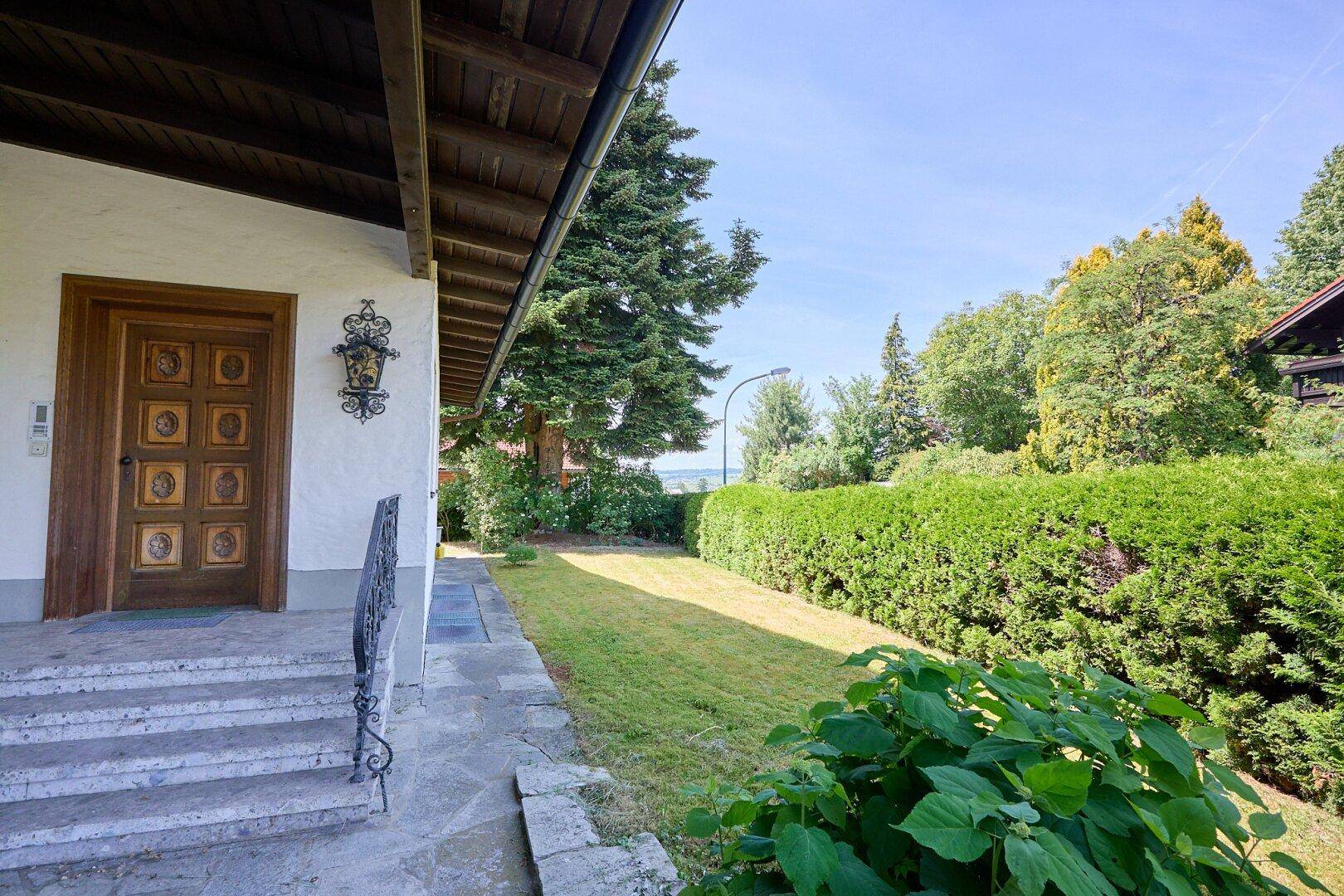 Eingangsbereich des Hauses mit Steintreppe, Holztür und gepflegter Hecke im Vorgarten.