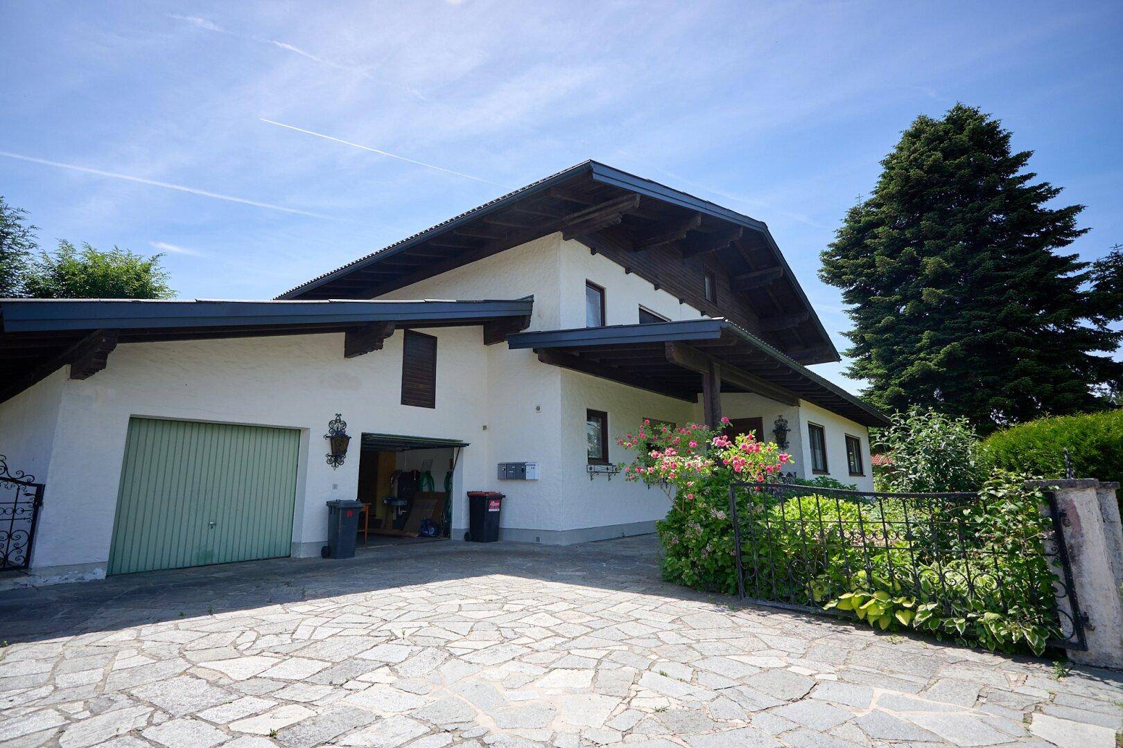Ansicht des Hauses mit Garage, breiter Zufahrt und traditioneller Architektur unter blauem Himmel.