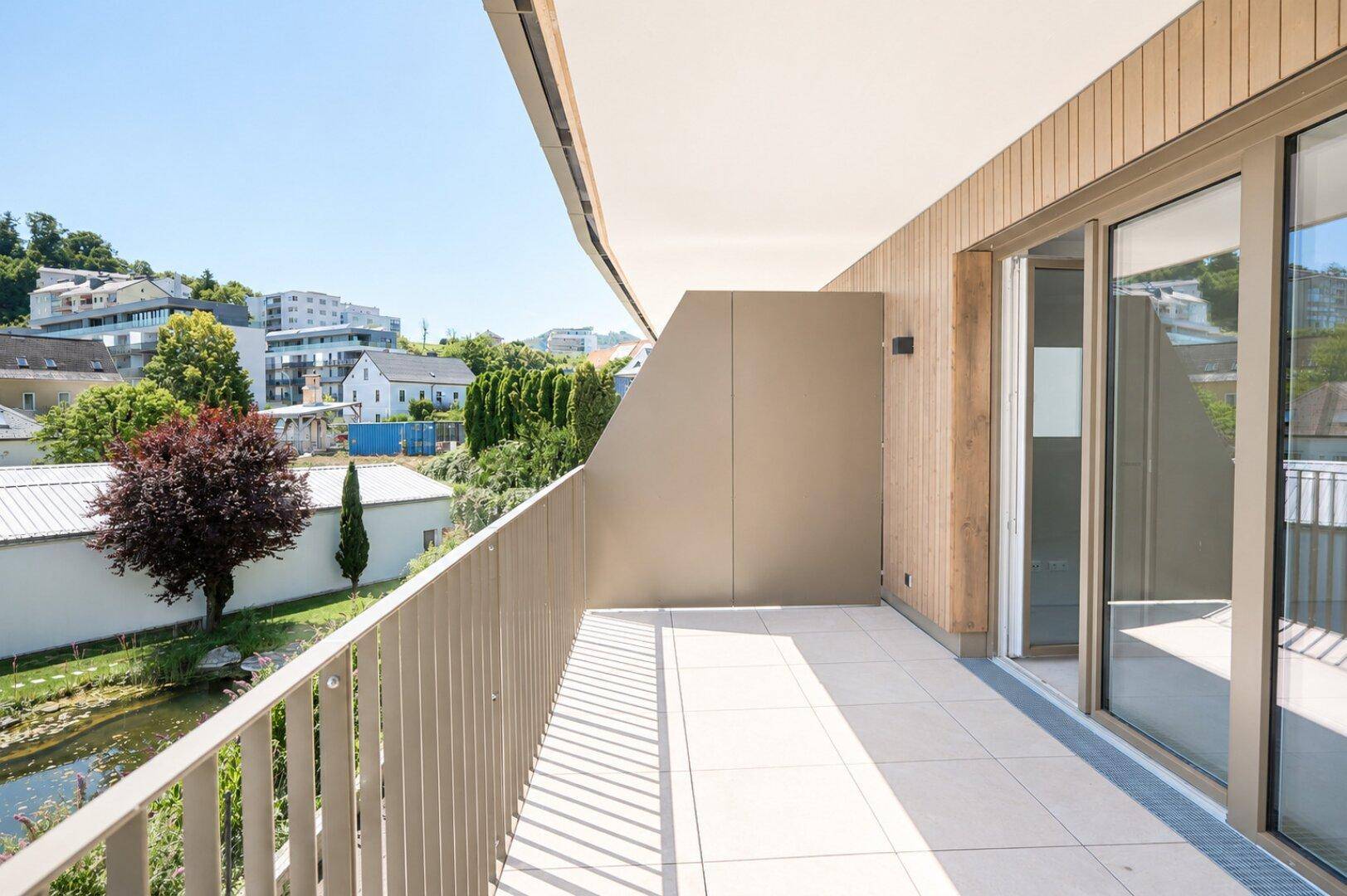 Moderner Balkon mit Fliesenboden und schöner Aussicht auf grüne Hügel und einen Teich.