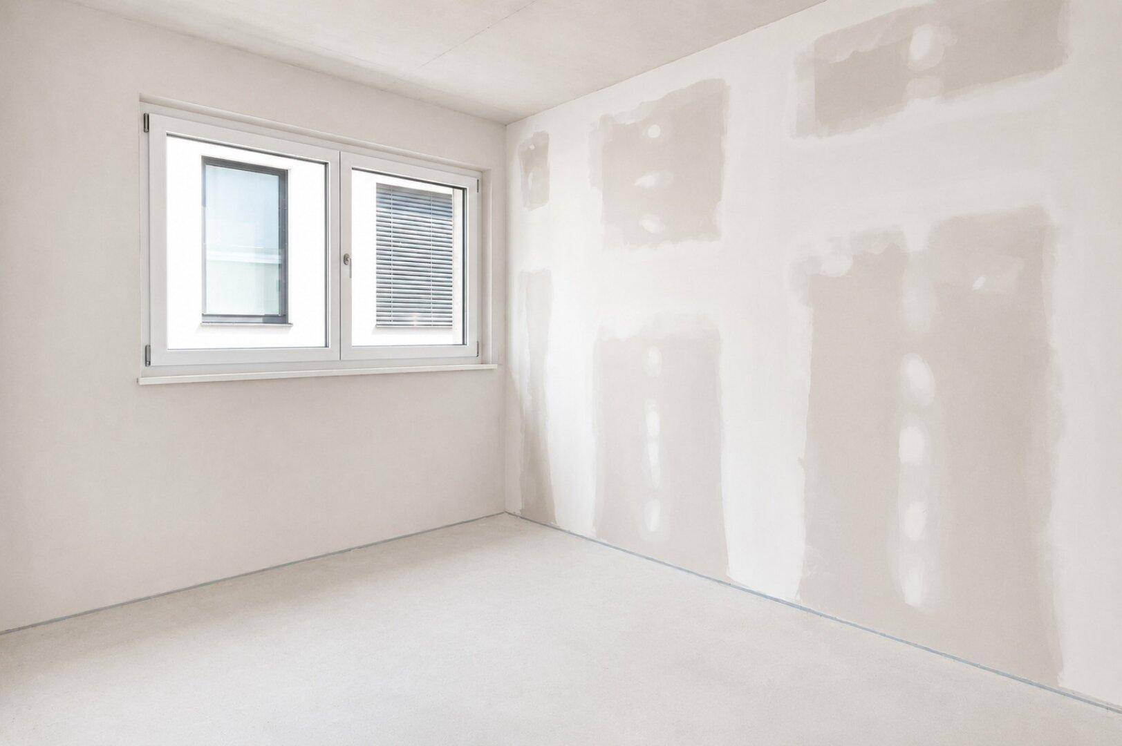 Unmöblierter Raum mit teilweise gespachtelten Wänden und einem Fenster mit Jalousien.