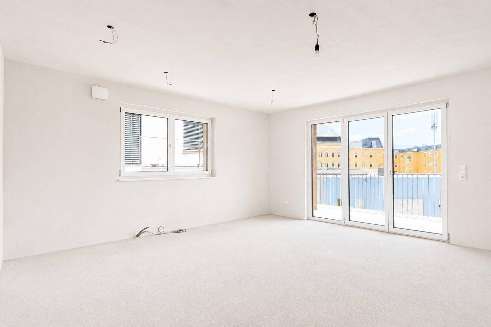 Heller, unmöblierter Raum mit großen Schiebetüren zum Balkon und Blick auf die Stadt.