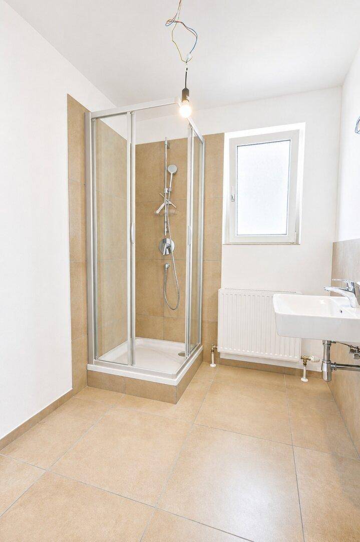 Modernes Badezimmer mit beigen Fliesen, Duschkabine, Waschbecken und Fenster.