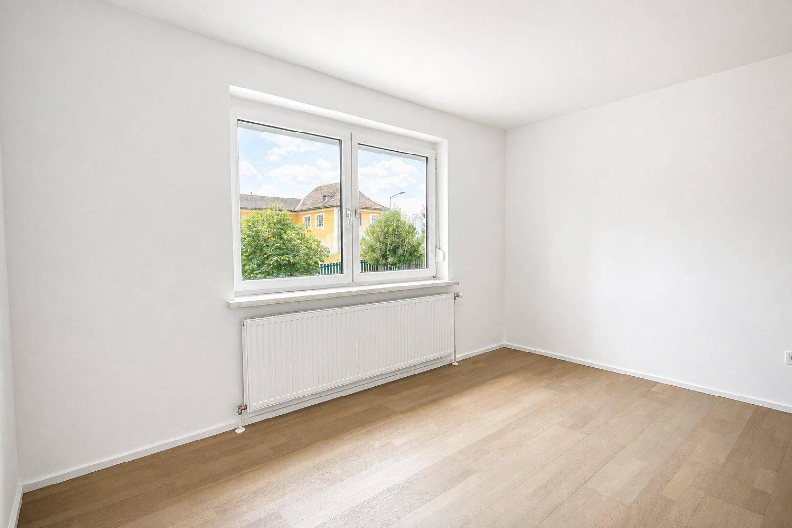 Ruhiges Zimmer mit Parkettboden, weiß gestrichenen Wänden und Fenster mit Blick ins Grüne.
