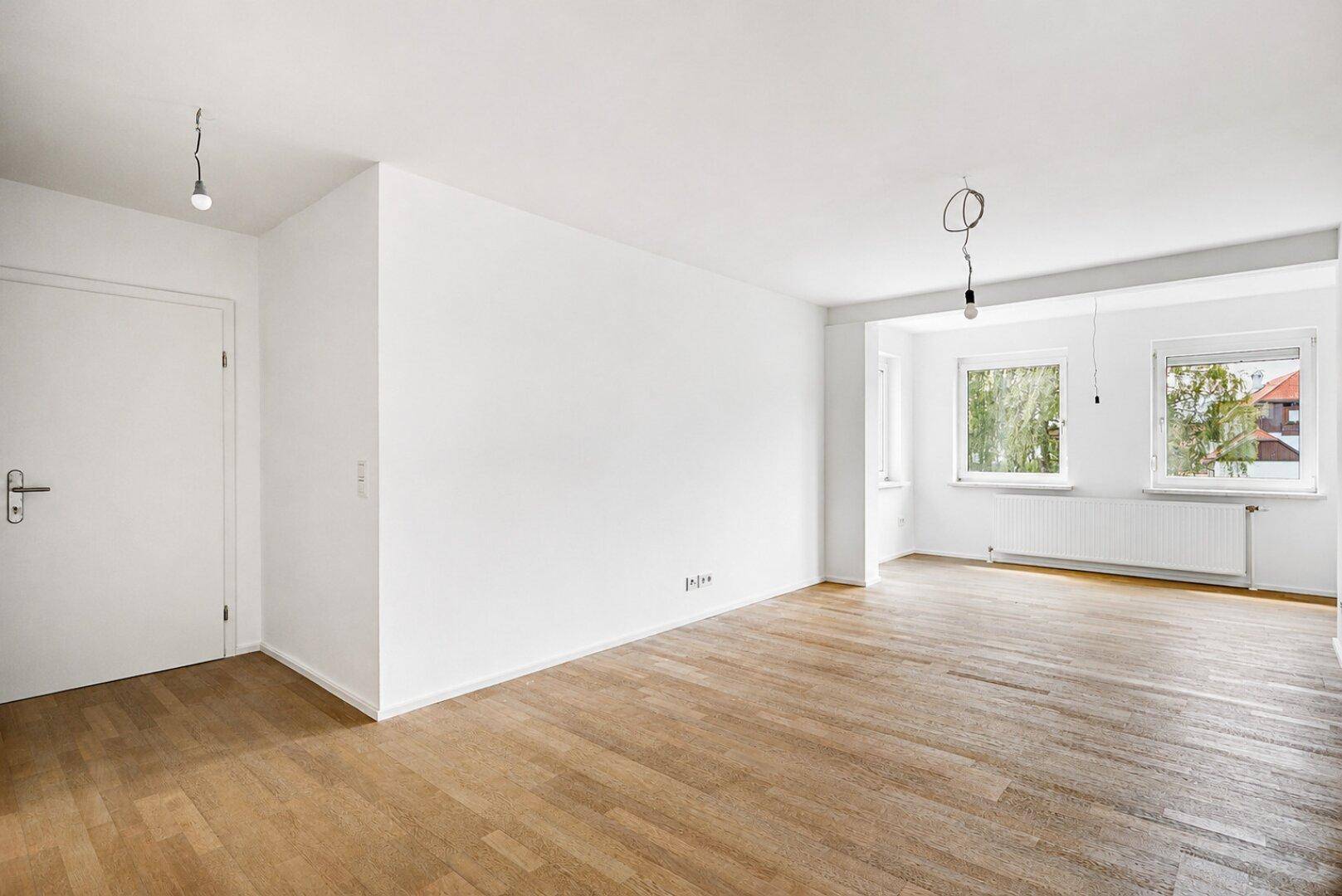 Geräumiger, heller Wohnbereich mit Parkettboden, weißen Wänden und mehreren Fenstern.