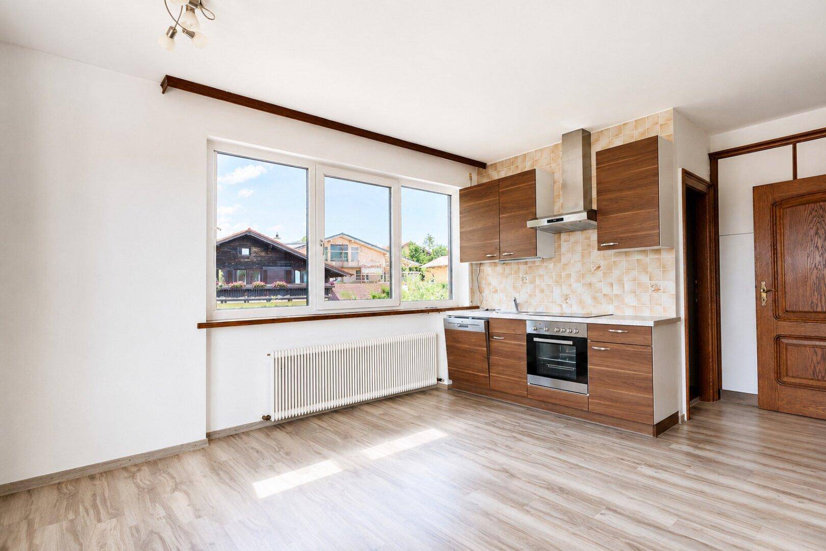 Moderne Einbauküche mit Holzschränken und integrierten Geräten in einem hellen Raum mit Fenster.