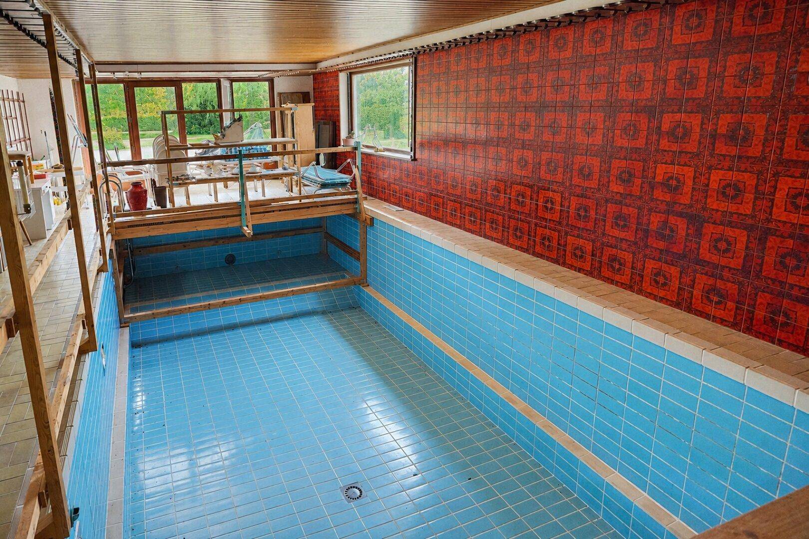 Innenpoolbereich mit blauen Fliesen und Holzverkleidung, bereit für die Nutzung als Wellnessbereich.