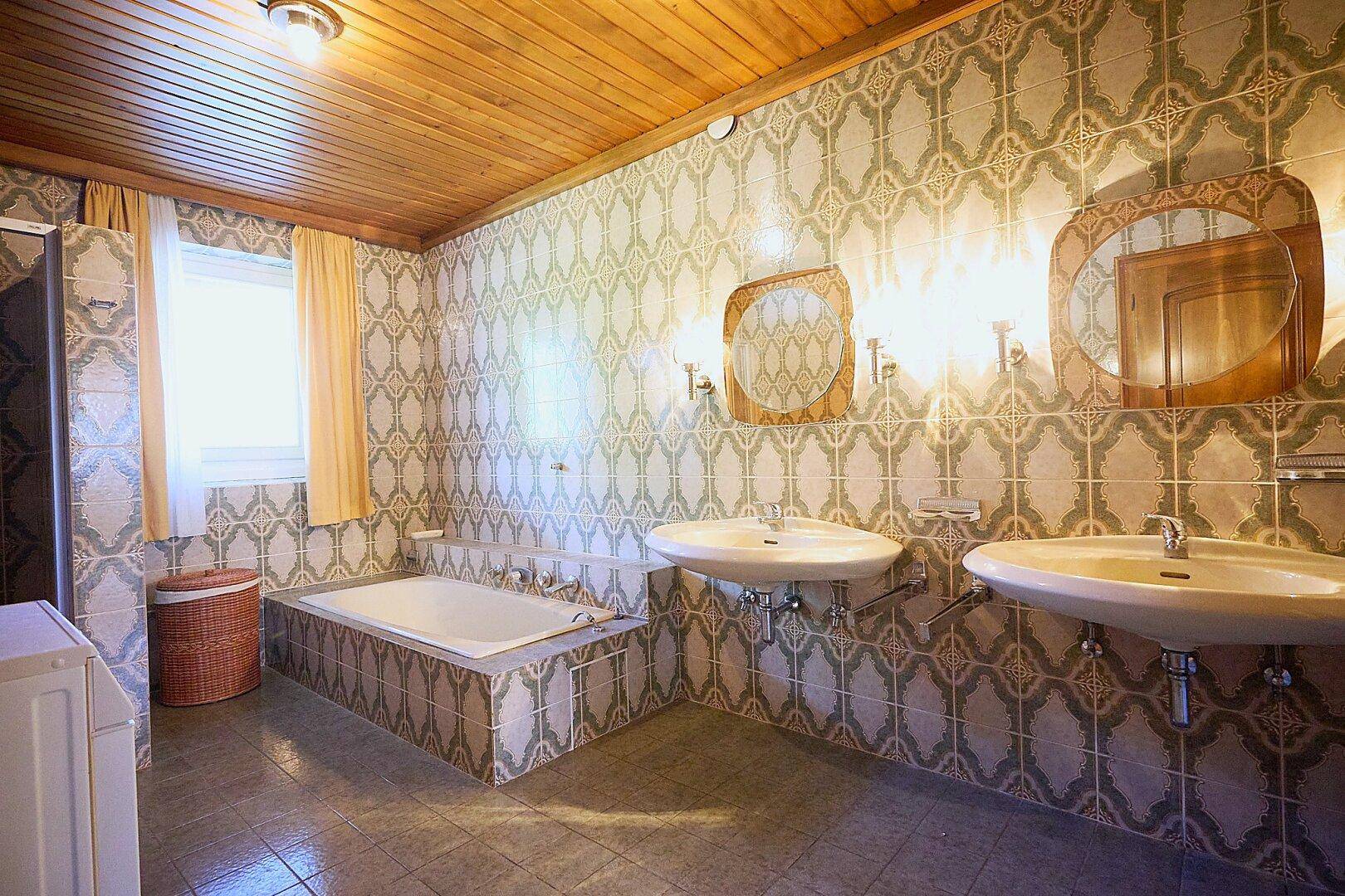 Badezimmer im 80er-Jahre-Stil mit gemusterten Fliesen, Doppelwaschbecken und Badewanne.