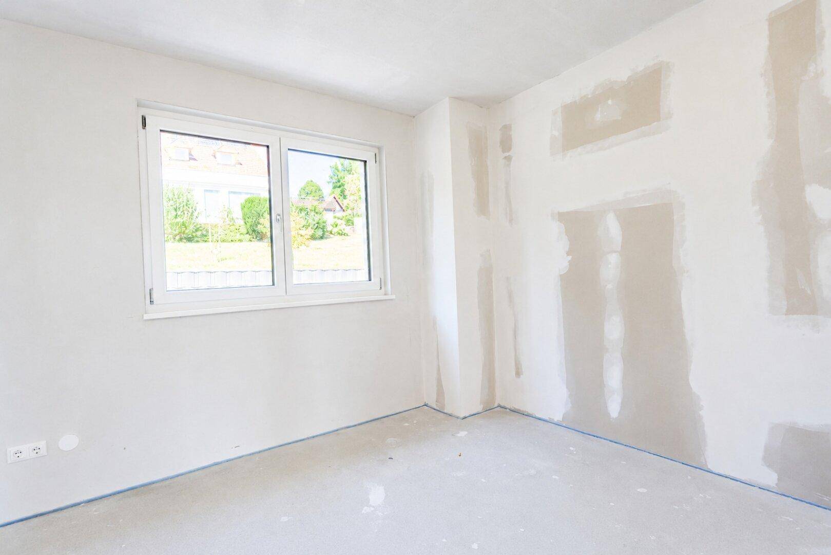 Unmöbliertes Zimmer im Neubau mit großem Fenster und viel natürlichem Lichteinfall.