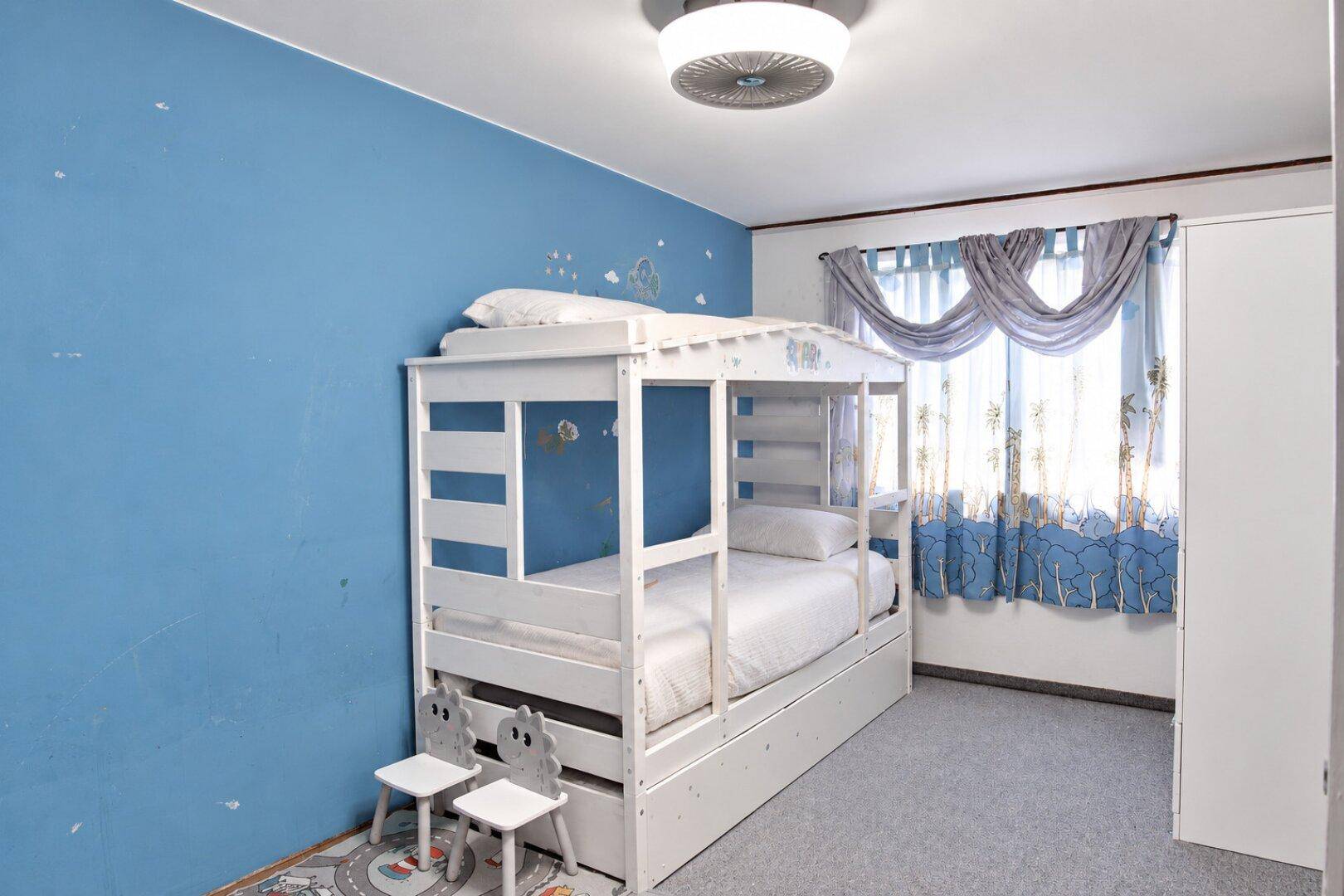 Kinderzimmer mit blau gestrichenen Wänden, einem weißen Etagenbett und Teppichboden.