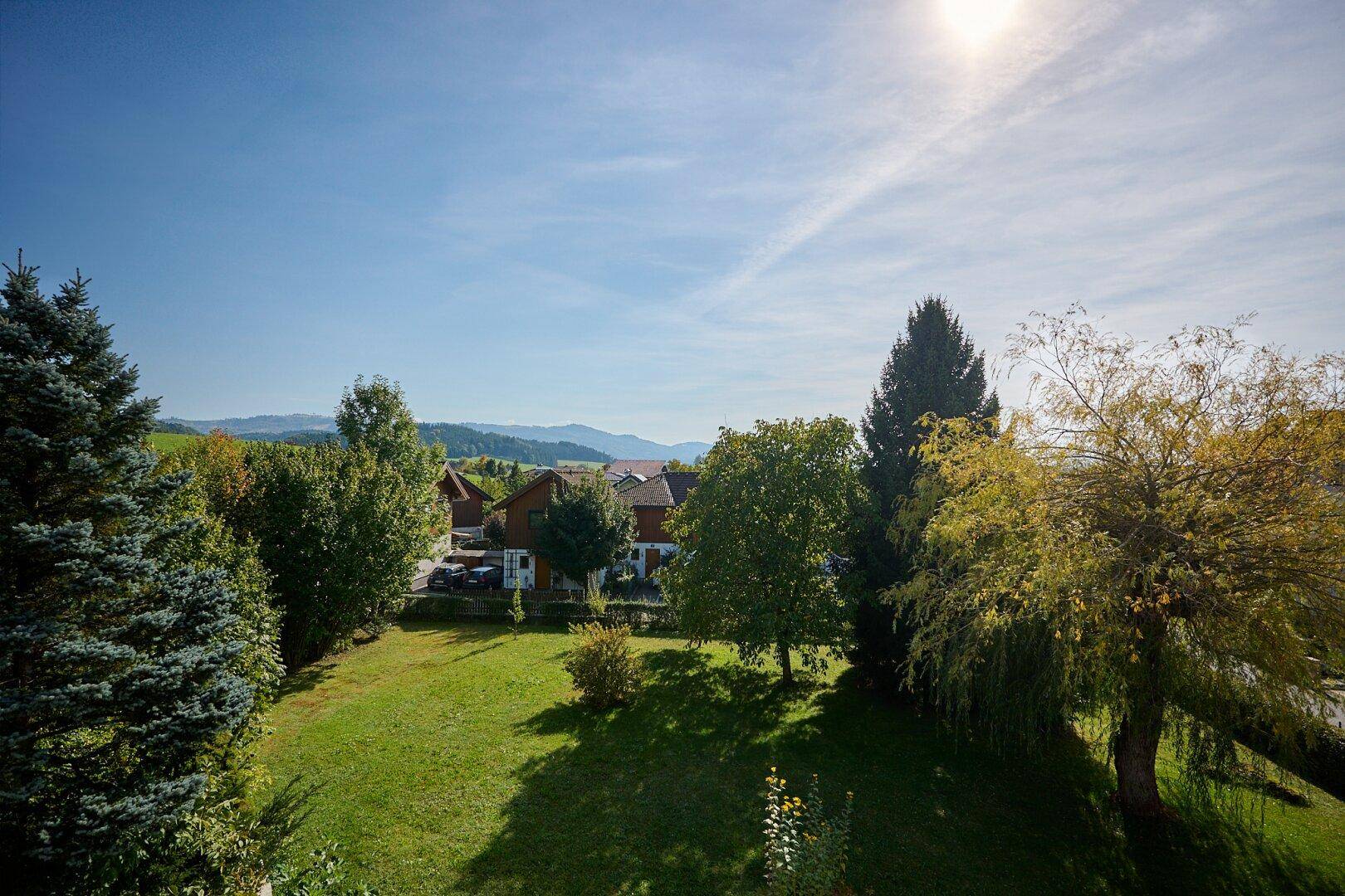 Weitläufiger Panoramablick über die Landschaft mit Häusern, Bäumen und fernen Bergen an einem sonnigen Tag.