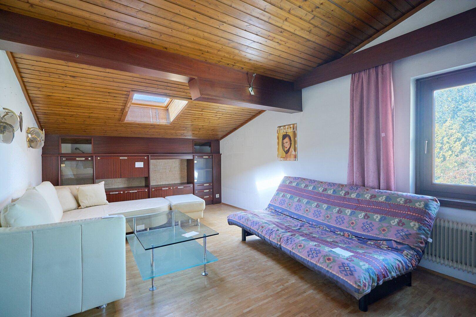 Gemütlicher Wohnbereich im Dachgeschoss mit Holzverkleidung, Dachfenster und rustikalem Charme.