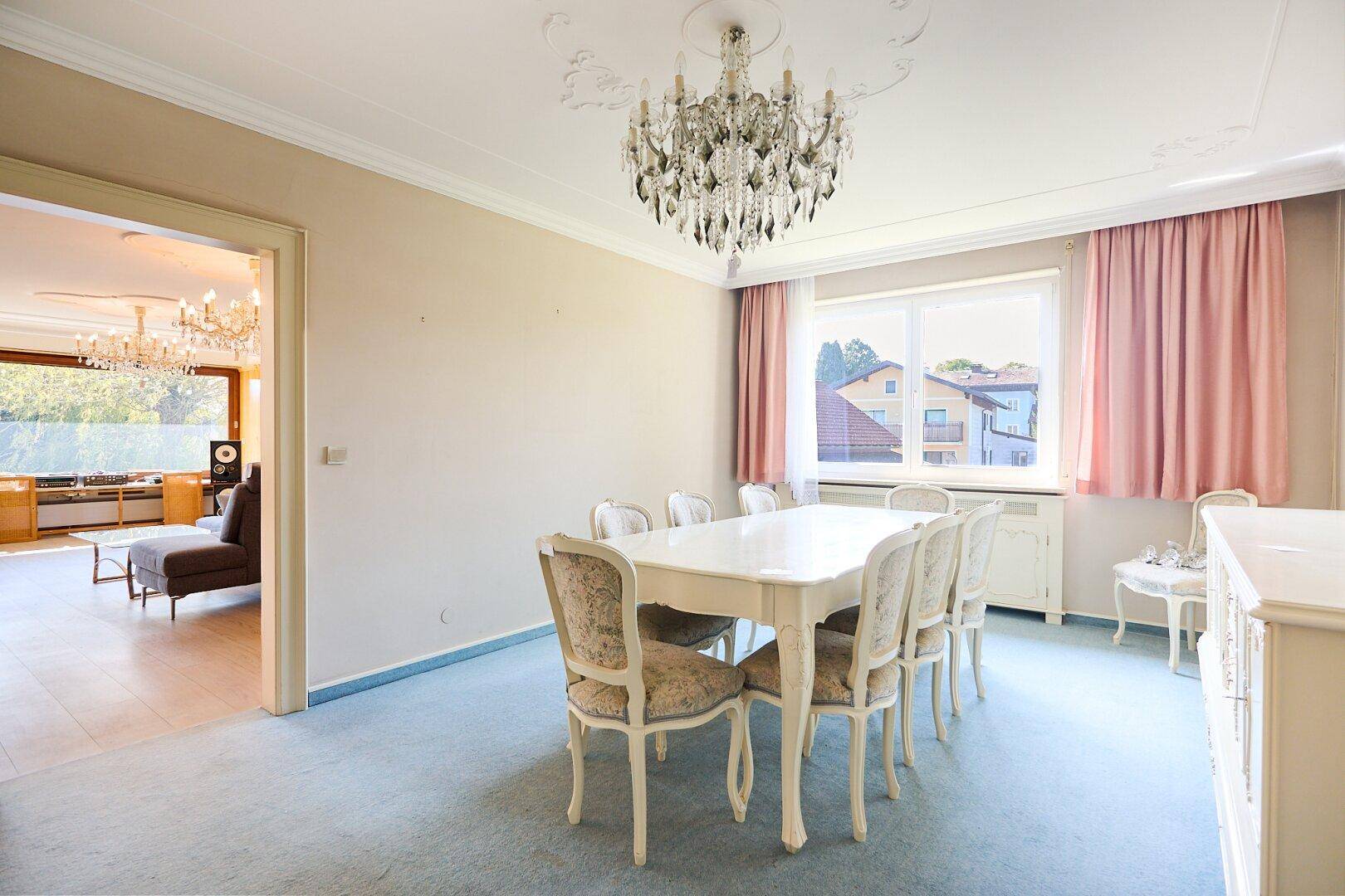Klassisches Esszimmer mit großem Esstisch, Kronleuchter und Blick ins Grüne durch das Fenster.