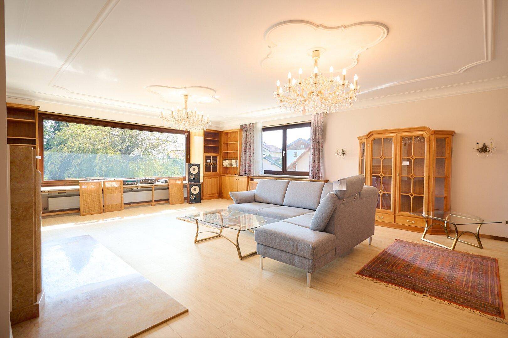 Helles Wohnzimmer mit bequemer Couch, Holzboden und großen Fenstern mit Blick ins Grüne.
