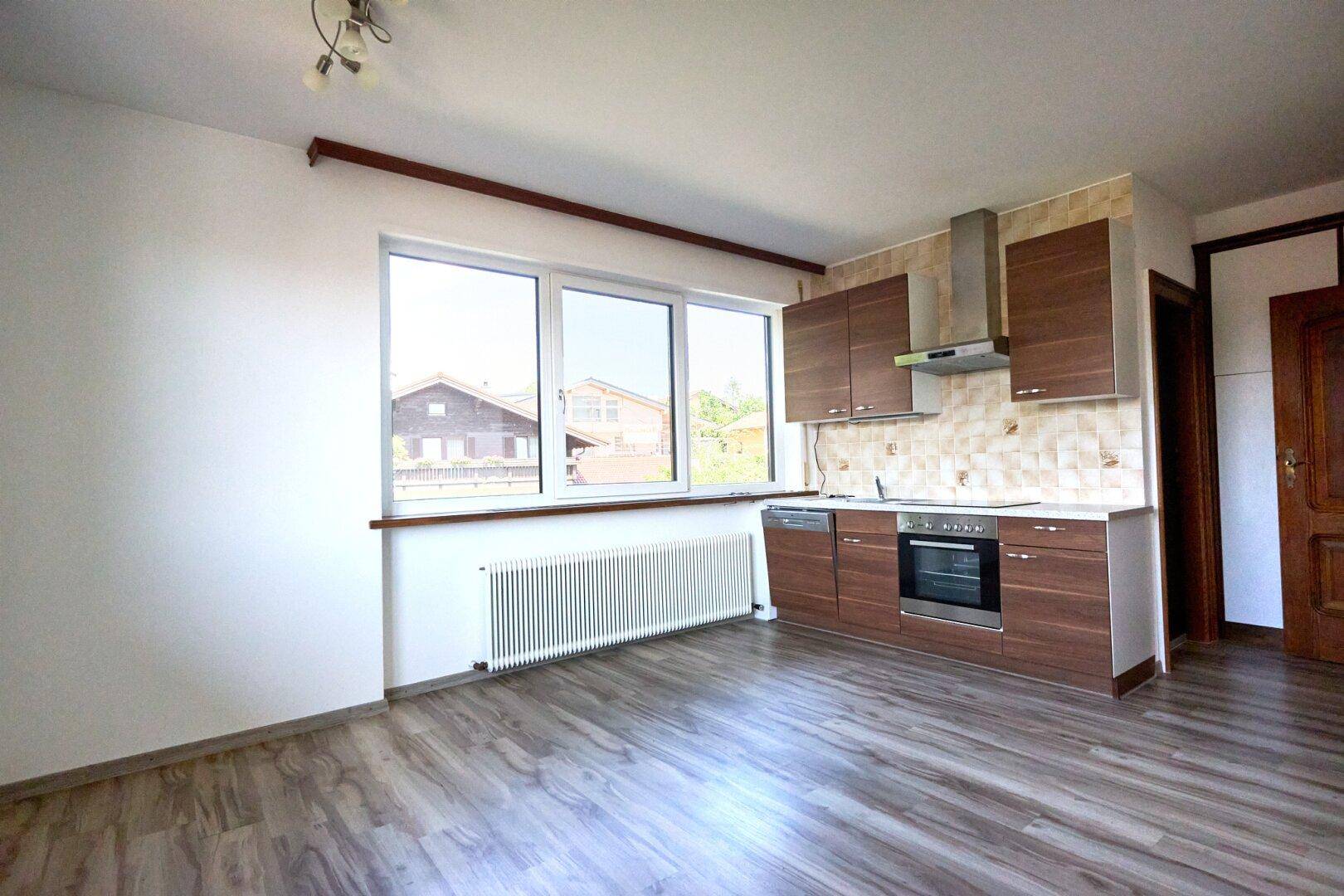 Kleine Küchenzeile mit braunen Schränken, integriertem Ofen und Fenster in einem hellen Raum.
