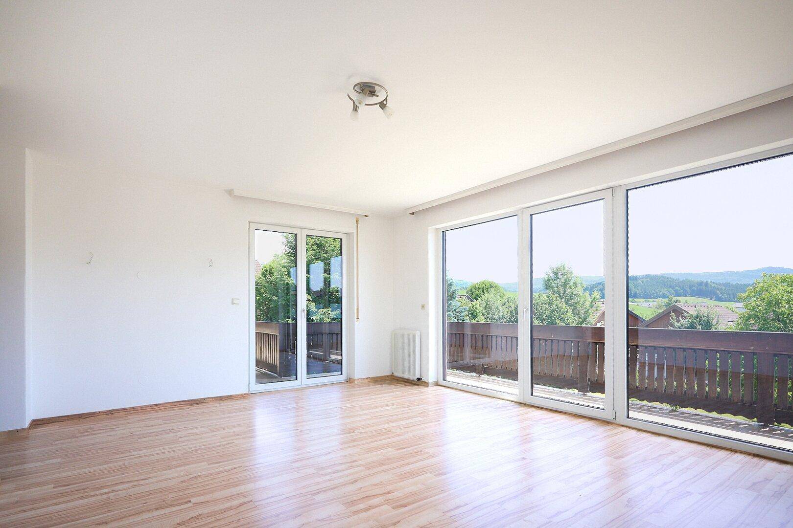 Heller Raum mit Holzboden und großen Schiebetüren, die zu einem Balkon mit Weitblick führen.